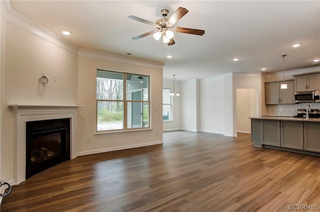 unfurnished living room with crown molding, sink, ceiling fan, and dark hardwood / wood-style flooring