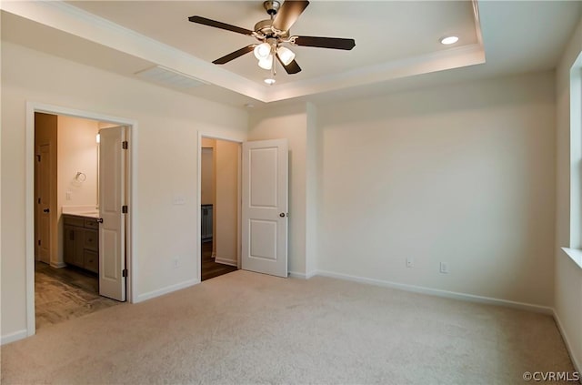 unfurnished bedroom featuring ensuite bath, a tray ceiling, and light carpet