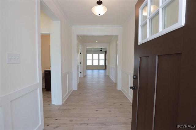 hall featuring a decorative wall, light wood-style floors, crown molding, and a wainscoted wall