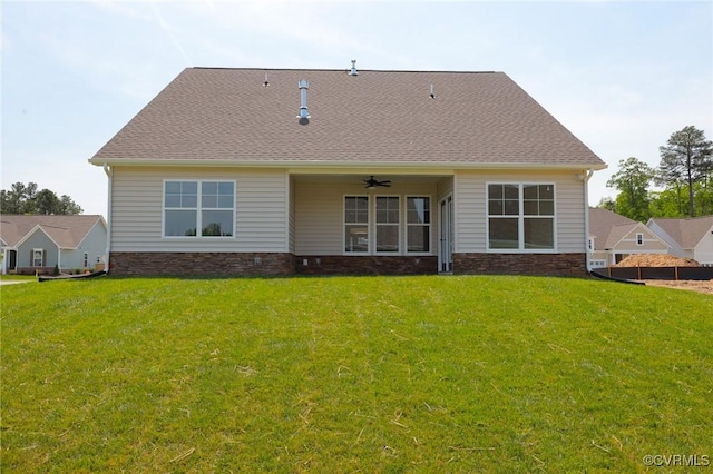 back of house with a yard, ceiling fan, stone siding, and roof with shingles