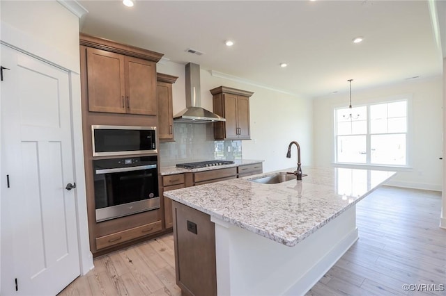 kitchen with appliances with stainless steel finishes, a sink, wall chimney range hood, decorative backsplash, and a kitchen island with sink