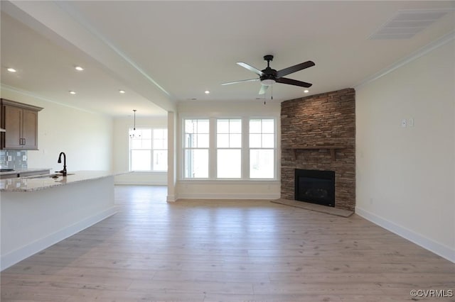 unfurnished living room featuring a sink, crown molding, ceiling fan, light wood-type flooring, and baseboards