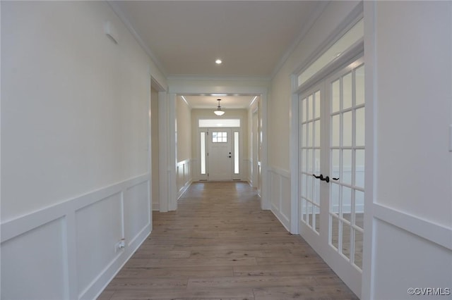 corridor featuring ornamental molding, a decorative wall, french doors, wood finished floors, and a wainscoted wall