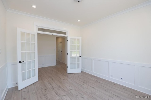 unfurnished room with french doors, crown molding, a decorative wall, wood finished floors, and wainscoting