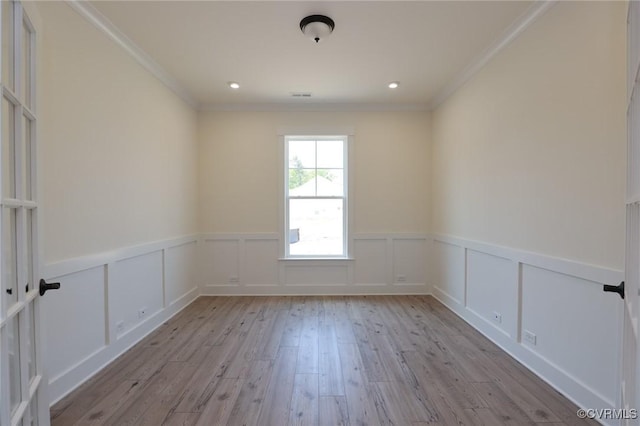 empty room with ornamental molding, a wainscoted wall, light wood finished floors, and a decorative wall