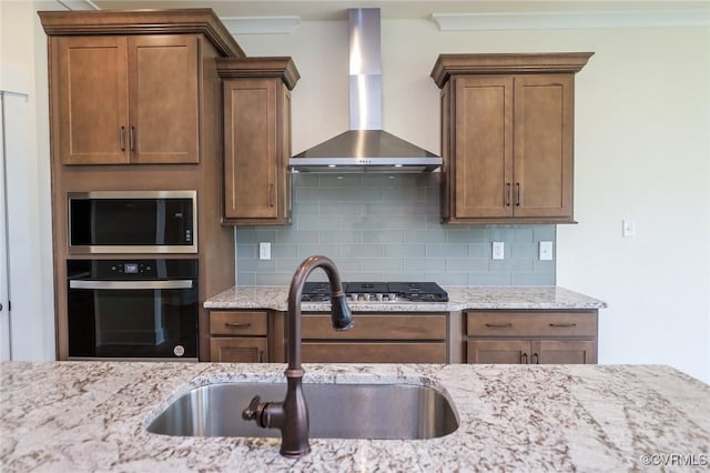 kitchen featuring appliances with stainless steel finishes, wall chimney exhaust hood, a sink, and backsplash