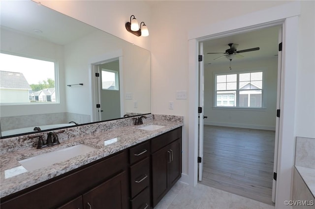 bathroom featuring a ceiling fan, double vanity, a bath, and baseboards