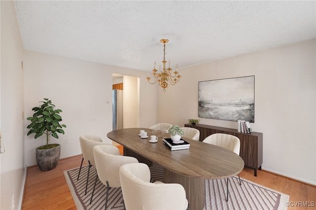 dining area with light hardwood / wood-style flooring, a textured ceiling, and a notable chandelier