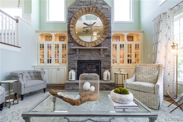 living area with ceiling fan, a stone fireplace, a towering ceiling, and a wealth of natural light