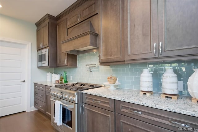 kitchen with appliances with stainless steel finishes, backsplash, dark hardwood / wood-style flooring, light stone counters, and custom range hood