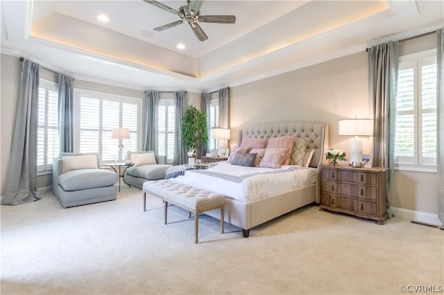 bedroom featuring ceiling fan, multiple windows, light carpet, and a tray ceiling