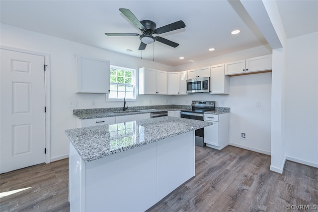 kitchen with white cabinets, light stone counters, appliances with stainless steel finishes, a kitchen island, and light wood-type flooring