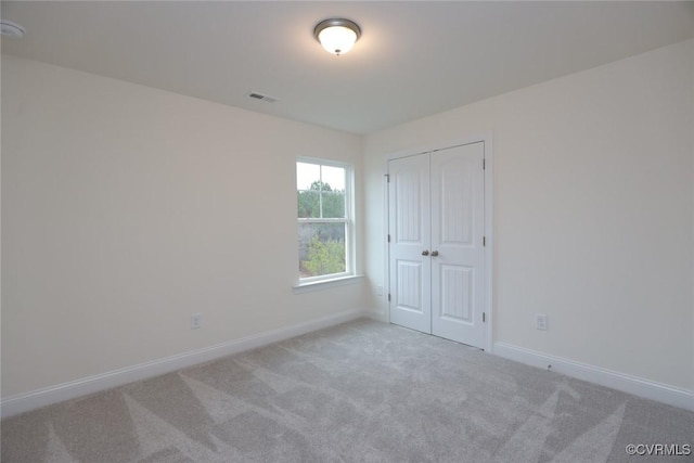 unfurnished bedroom with light colored carpet and a closet