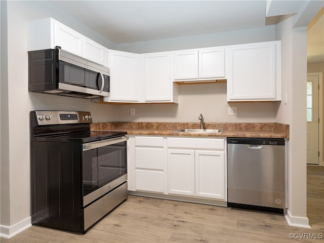 kitchen with stainless steel appliances, sink, white cabinetry, and light hardwood / wood-style floors