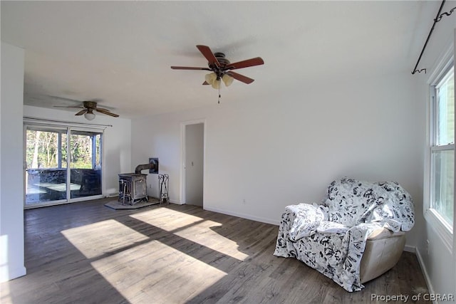 sitting room featuring a wood stove, ceiling fan, and dark wood-type flooring