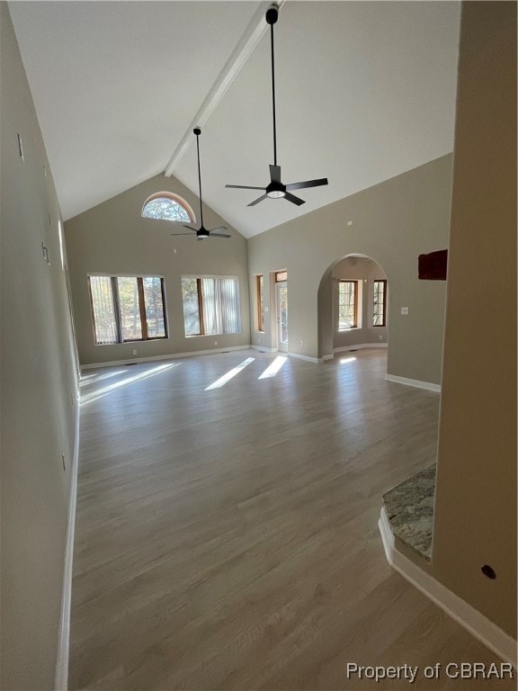 unfurnished living room featuring ceiling fan, plenty of natural light, beamed ceiling, and hardwood / wood-style flooring