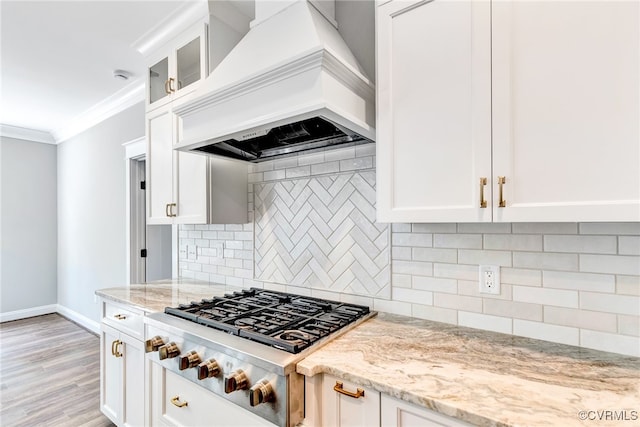 kitchen featuring light stone counters, custom exhaust hood, backsplash, stainless steel gas stovetop, and light wood-type flooring