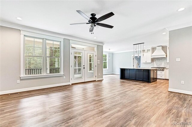 unfurnished living room featuring light hardwood / wood-style floors, ceiling fan, sink, and crown molding