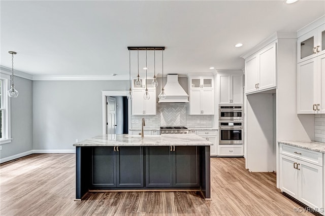 kitchen with light stone counters, white cabinets, backsplash, light wood-type flooring, and custom exhaust hood