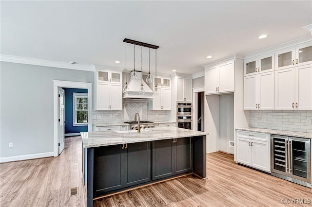 kitchen featuring white cabinets, premium range hood, beverage cooler, light stone countertops, and light hardwood / wood-style floors