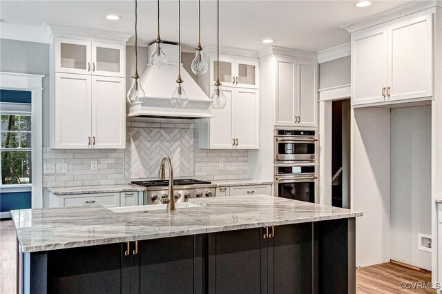 kitchen with a center island with sink, hanging light fixtures, and white cabinetry