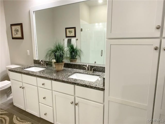 full bathroom featuring double vanity, a stall shower, a sink, and toilet