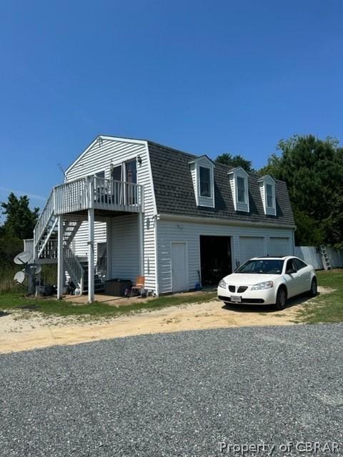 view of front of house with a gambrel roof, stairs, a deck, a garage, and driveway