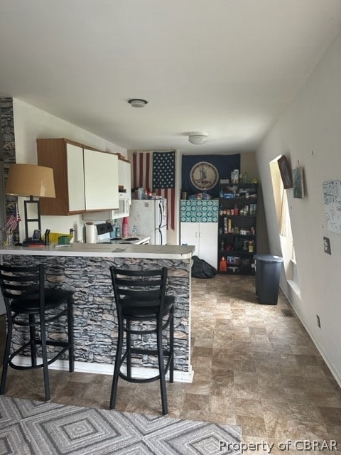 kitchen with light tile patterned flooring, white cabinetry, white appliances, kitchen peninsula, and a kitchen breakfast bar