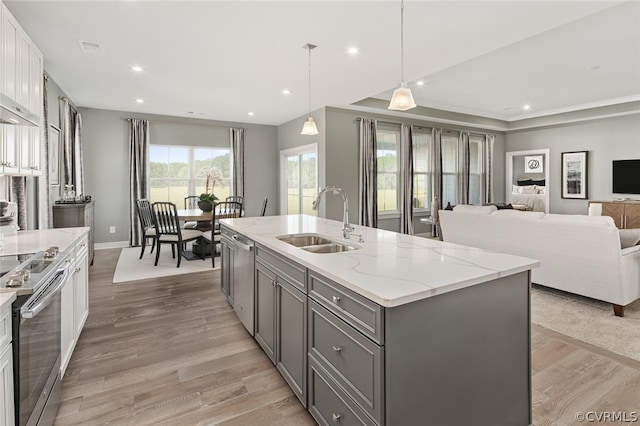 kitchen with sink, light hardwood / wood-style flooring, pendant lighting, and a kitchen island with sink