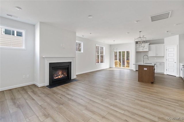 unfurnished living room with light wood-type flooring, sink, and a chandelier