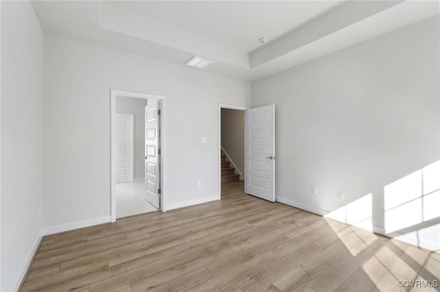 spare room featuring a raised ceiling and light hardwood / wood-style flooring