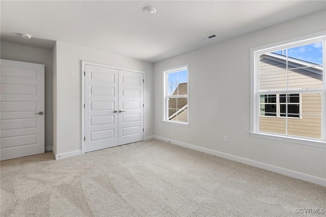 unfurnished bedroom with multiple windows, light carpet, and a closet