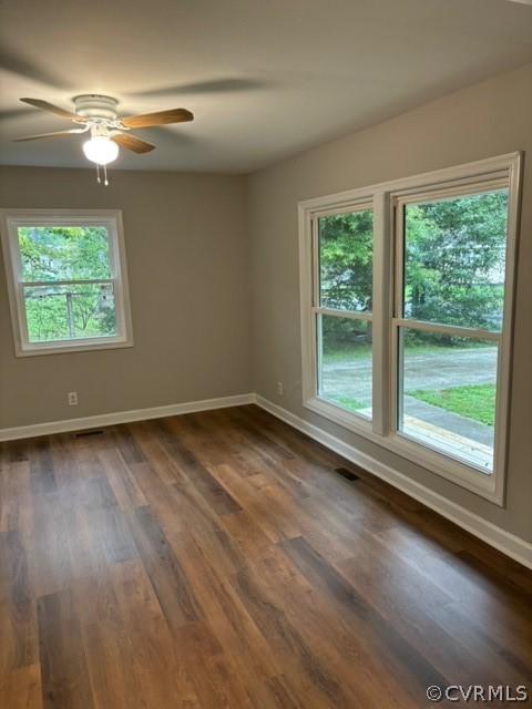 spare room featuring dark wood finished floors, a healthy amount of sunlight, and baseboards