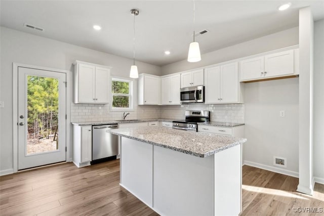 kitchen with appliances with stainless steel finishes, light stone counters, a center island, white cabinets, and hanging light fixtures