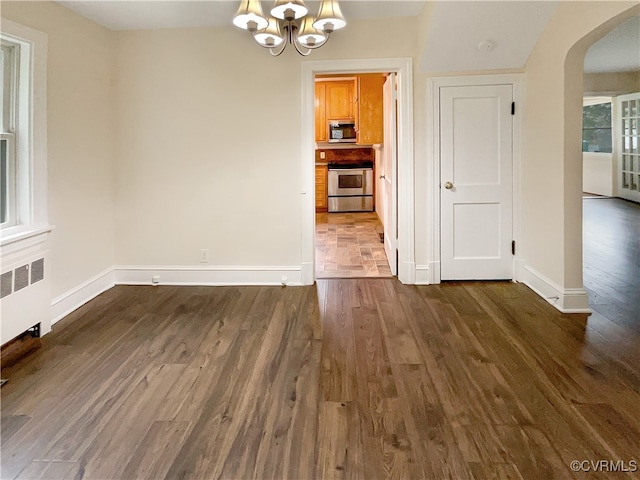 unfurnished dining area featuring a chandelier, radiator heating unit, and dark hardwood / wood-style floors