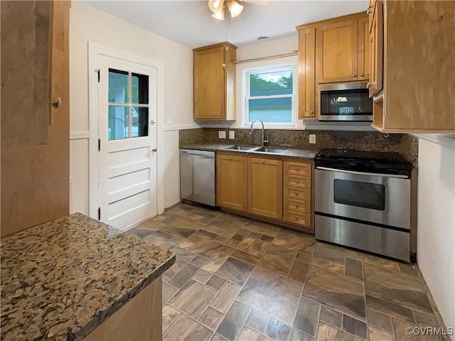 kitchen featuring appliances with stainless steel finishes, dark stone countertops, ceiling fan, and sink