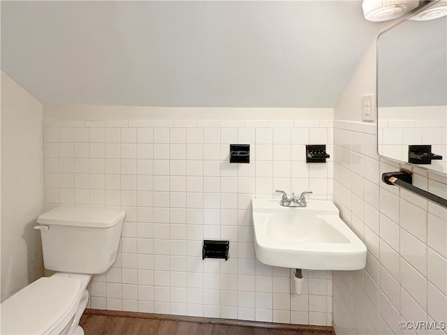 bathroom with lofted ceiling, wood-type flooring, sink, tile walls, and toilet