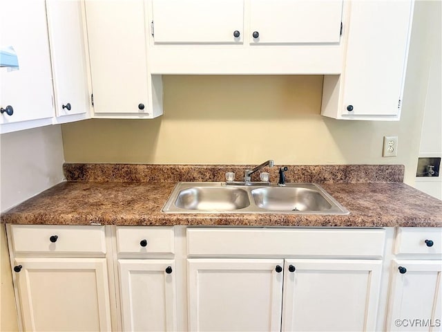 kitchen featuring dark countertops, a sink, and white cabinets