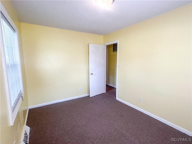 empty room with visible vents, dark carpet, a textured ceiling, and baseboards