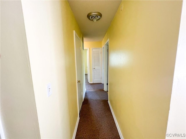 hall featuring baseboards and dark colored carpet