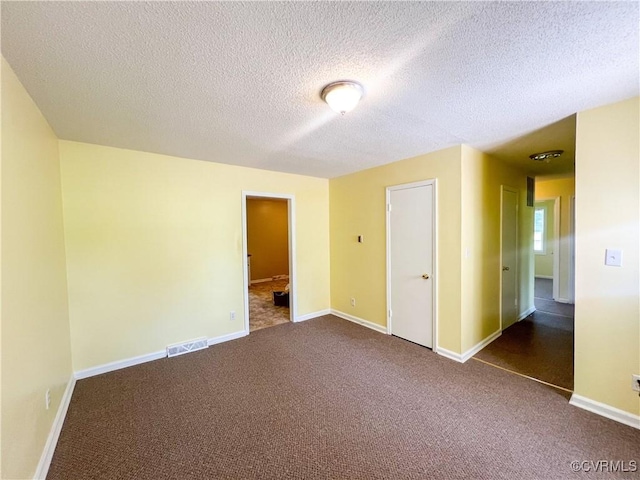 spare room featuring carpet floors, visible vents, a textured ceiling, and baseboards