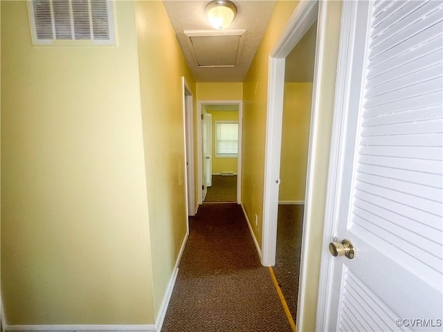 hall featuring dark colored carpet, attic access, visible vents, and baseboards