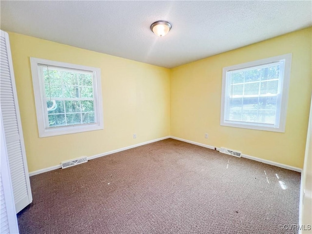 unfurnished room with a textured ceiling, dark carpet, visible vents, and baseboards