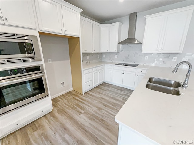 kitchen featuring backsplash, stainless steel appliances, light hardwood / wood-style floors, wall chimney exhaust hood, and sink