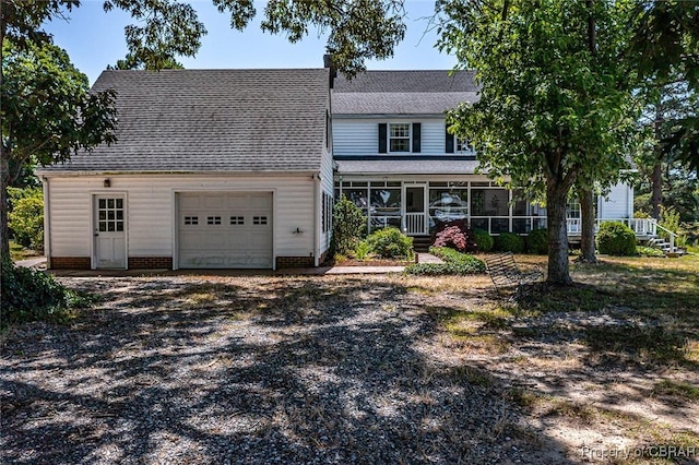 view of front facade with dirt driveway, roof with shingles, and a sunroom