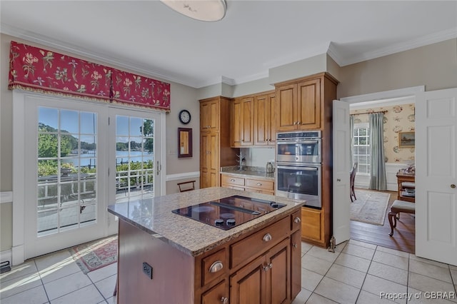 kitchen with black electric cooktop, light tile patterned floors, double oven, a water view, and a center island