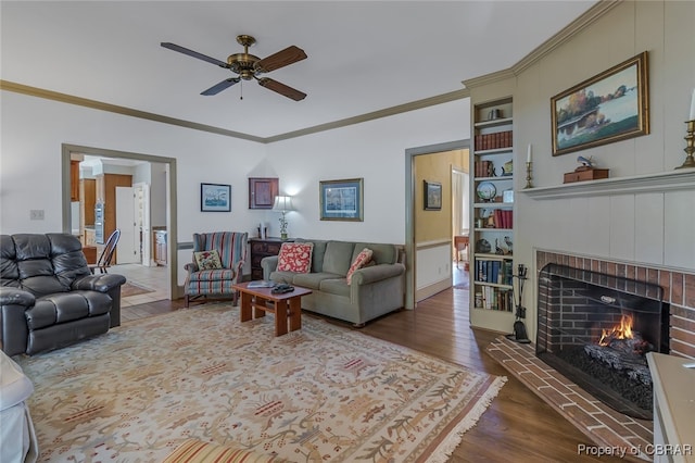 living room with a fireplace, dark hardwood / wood-style flooring, built in shelves, ornamental molding, and ceiling fan