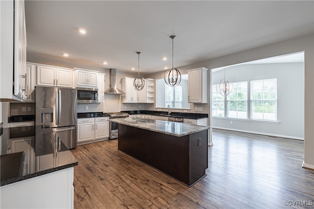 kitchen with stainless steel appliances, a center island, an inviting chandelier, hanging light fixtures, and wall chimney range hood