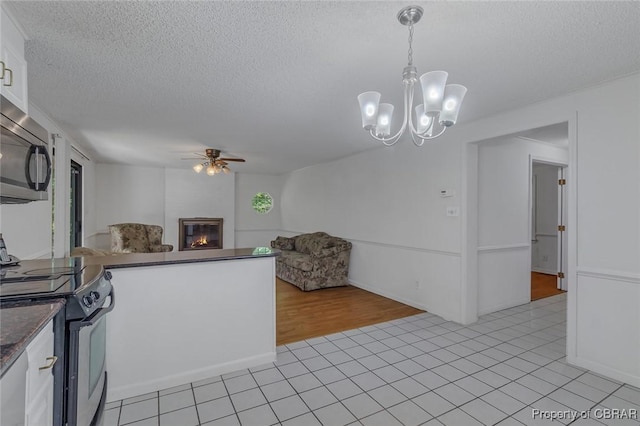 kitchen with appliances with stainless steel finishes, a glass covered fireplace, dark countertops, ceiling fan with notable chandelier, and open floor plan