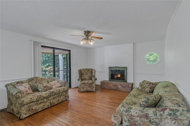 living room with a textured ceiling, a fireplace, ceiling fan, and hardwood / wood-style floors